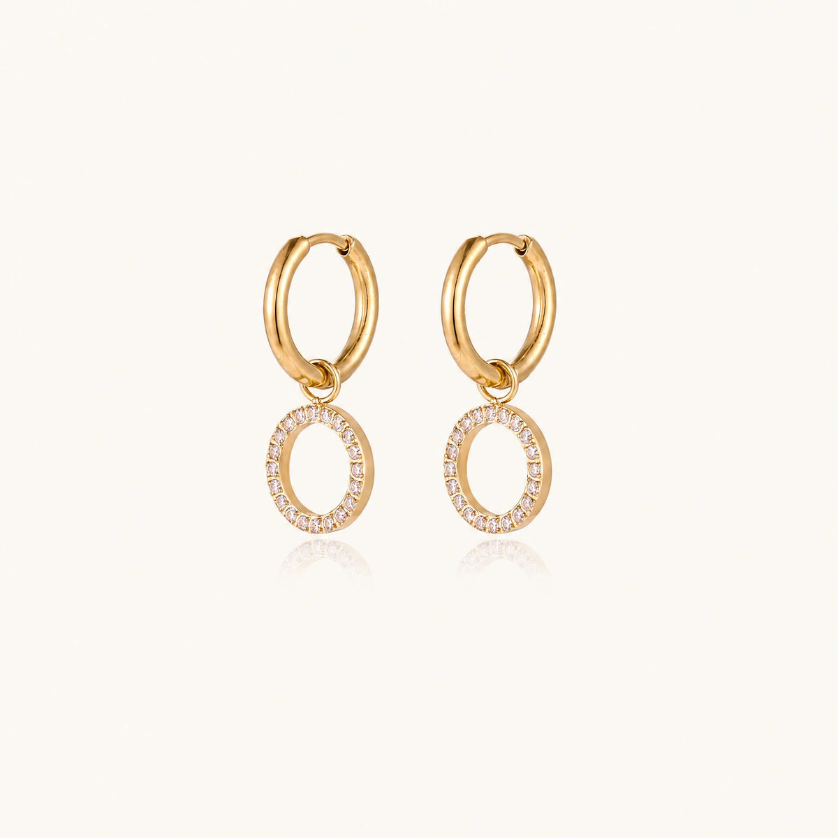 Gold-plated huggie hoop earrings with CZ-studded open circle charms on beige background