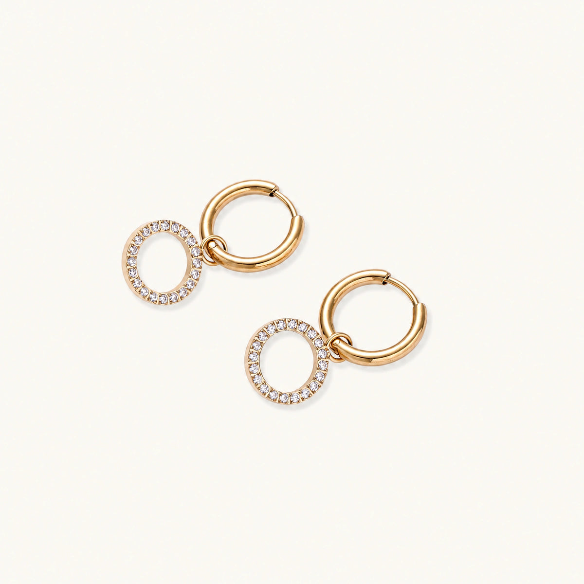Gold-plated huggie hoop earrings with CZ-studded open circle charms on beige background
