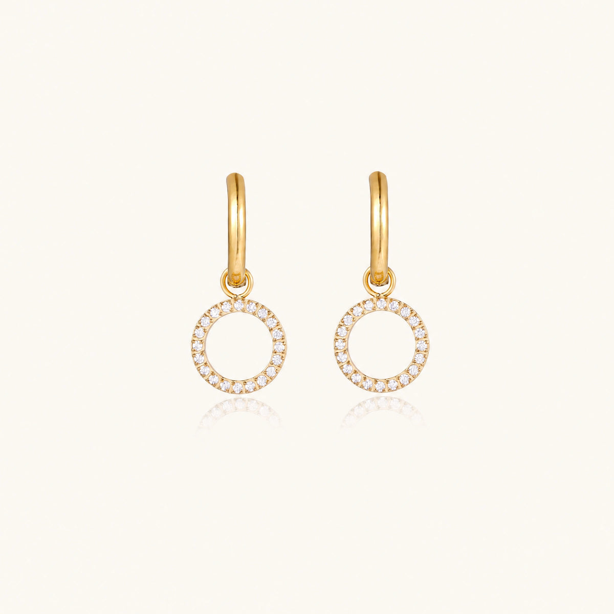 Gold-plated huggie hoop earrings with CZ-studded open circle charms on beige background