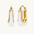 Sculptural gold-plated hoop earrings with flowing curved design and lever-back closure on cream background.