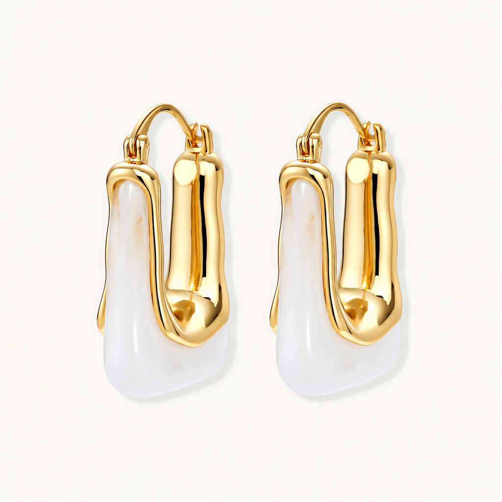 Sculptural gold-plated hoop earrings with flowing curved design and lever-back closure on cream background.