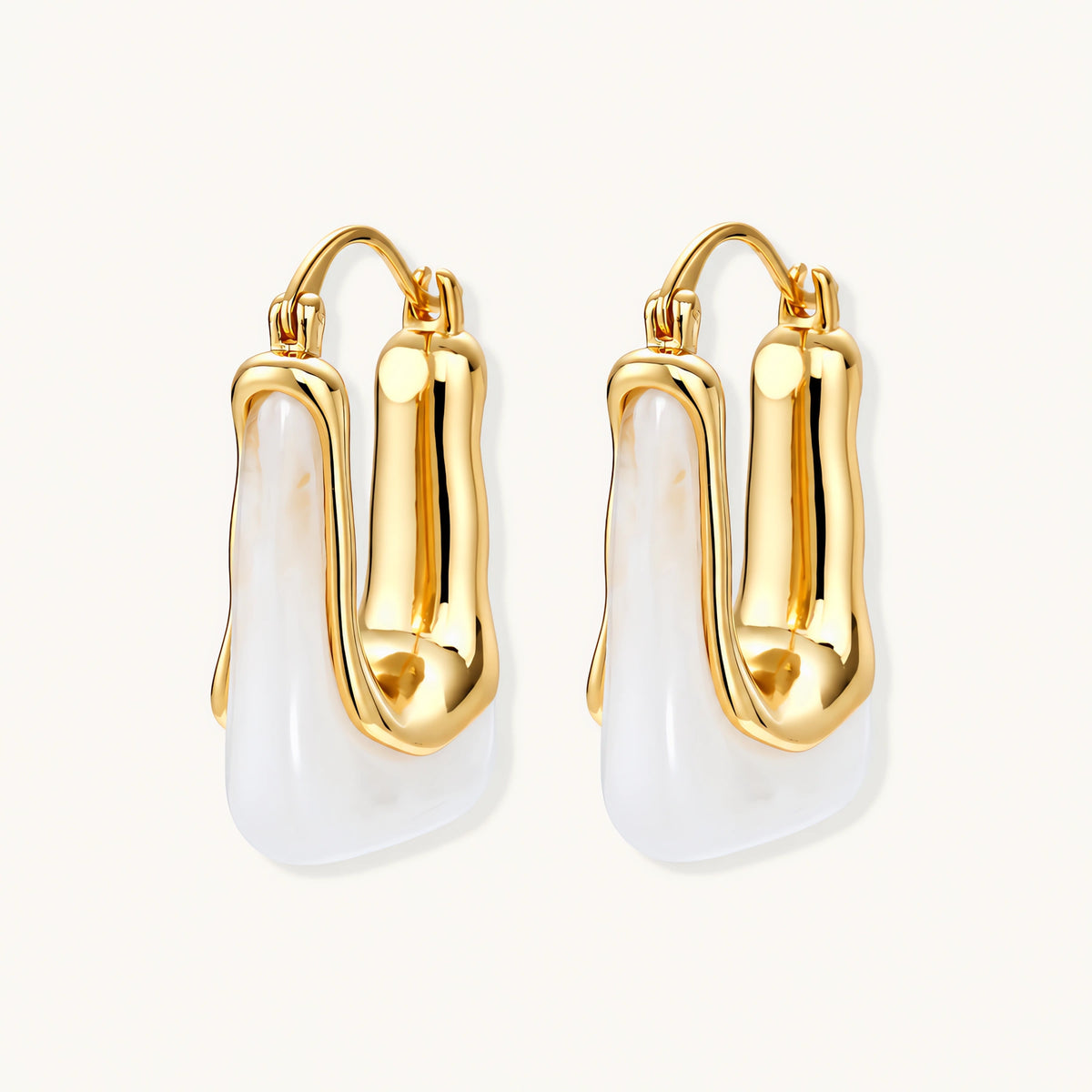 Sculptural gold-plated hoop earrings with flowing curved design and lever-back closure on cream background.