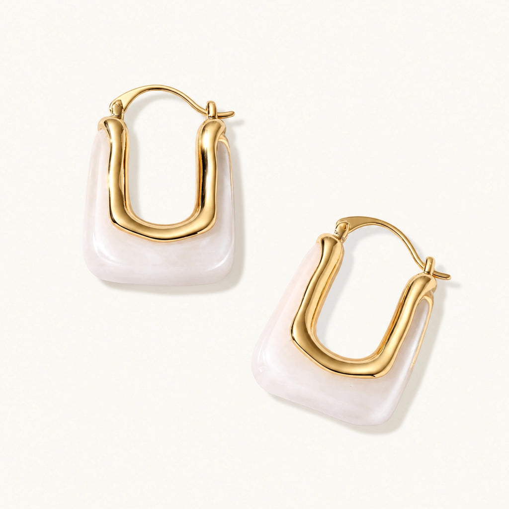 Sculptural gold-plated hoop earrings with flowing curved design and lever-back closure on cream background.