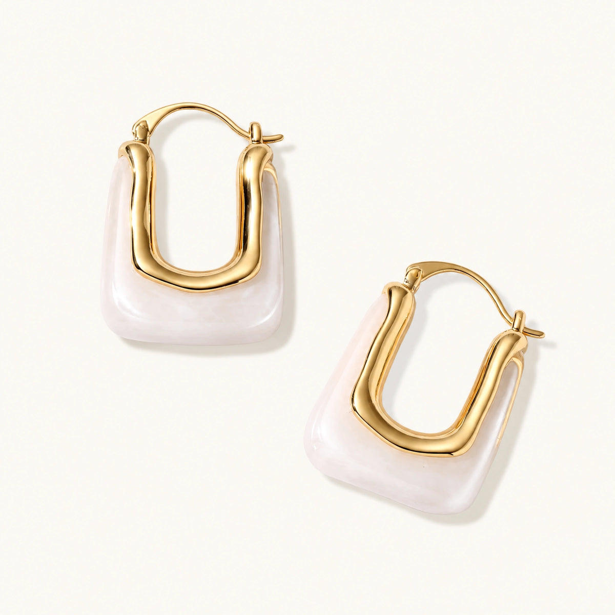 Sculptural gold-plated hoop earrings with flowing curved design and lever-back closure on cream background.
