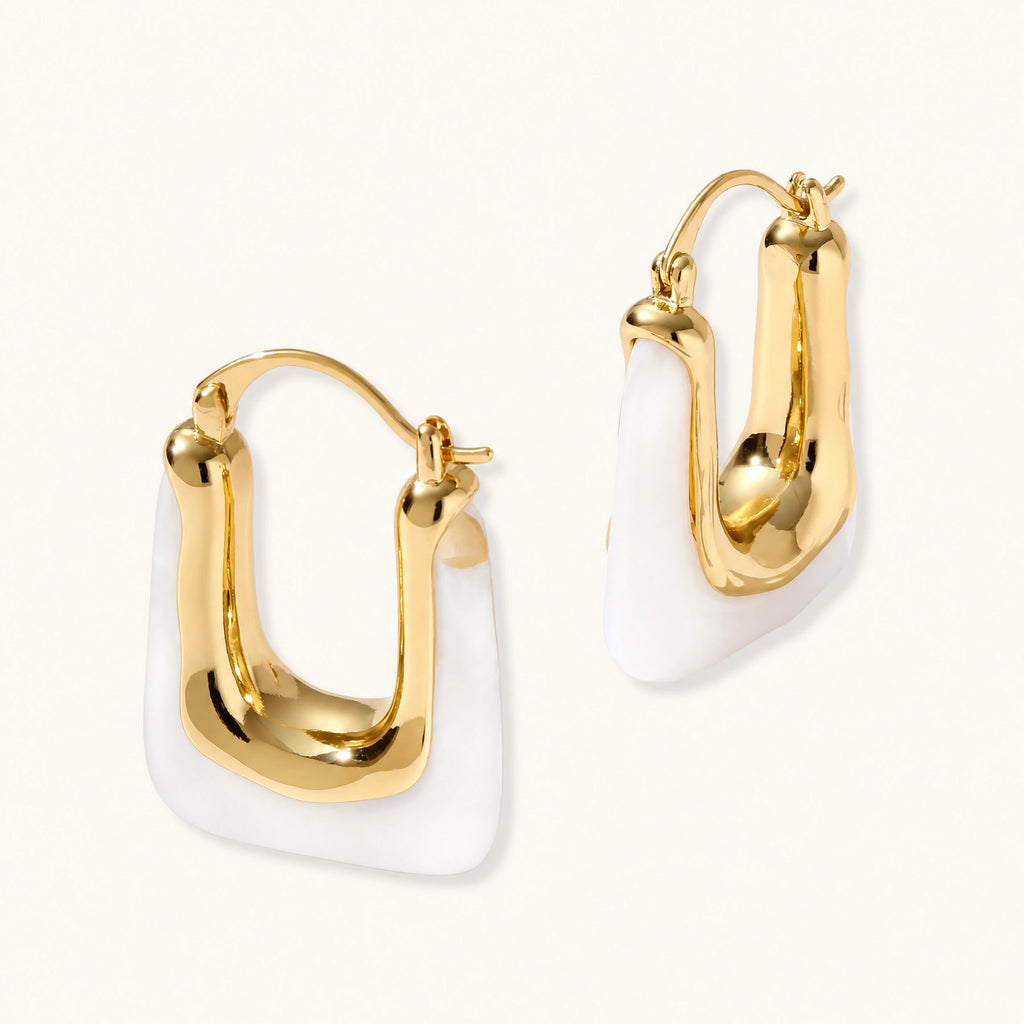 Sculptural gold-plated hoop earrings with flowing curved design and lever-back closure on cream background.