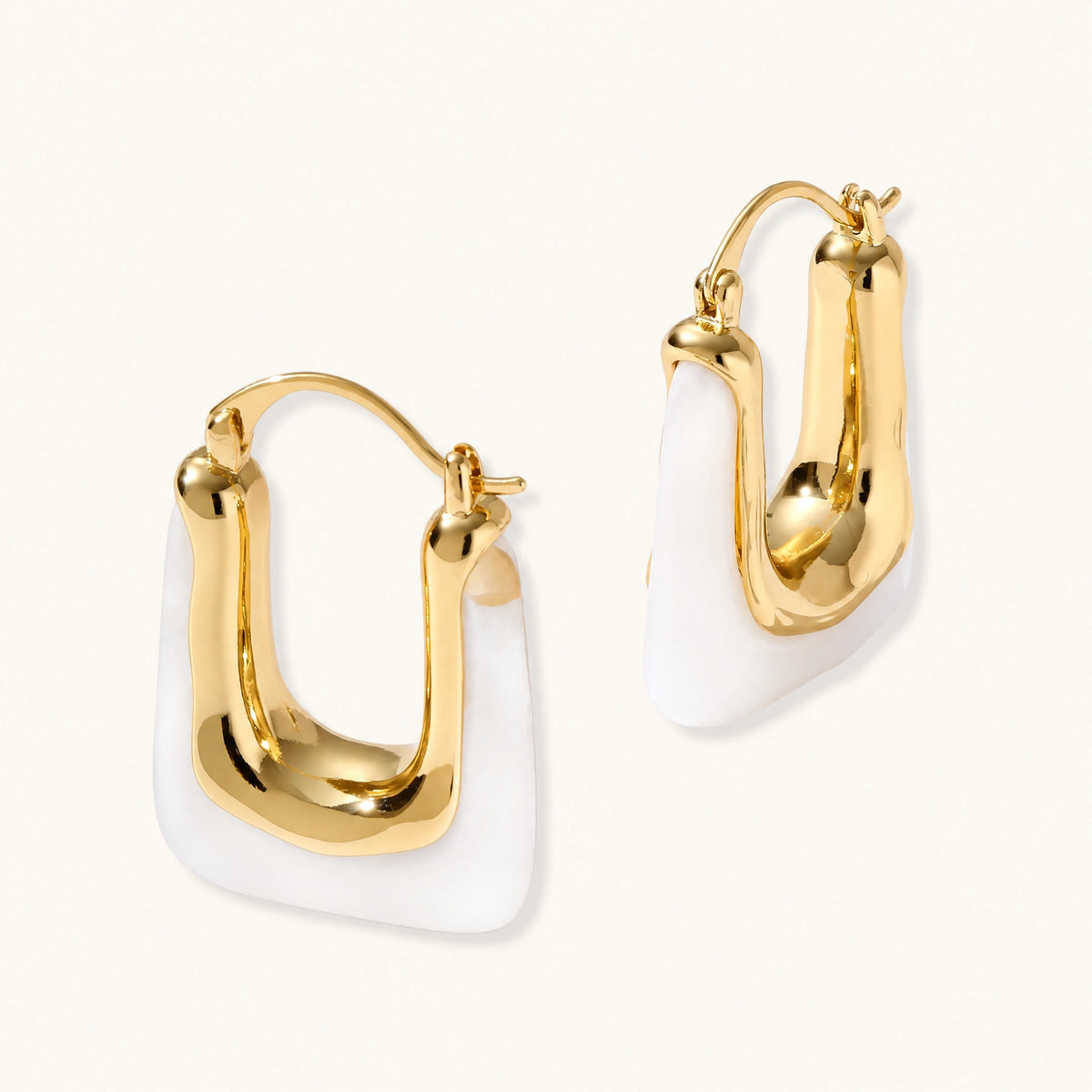 Sculptural gold-plated hoop earrings with flowing curved design and lever-back closure on cream background.